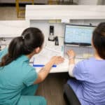 Two women in scrubs staring at a computer monitor