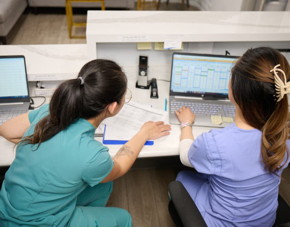 Two women in scrubs staring at a computer monitor