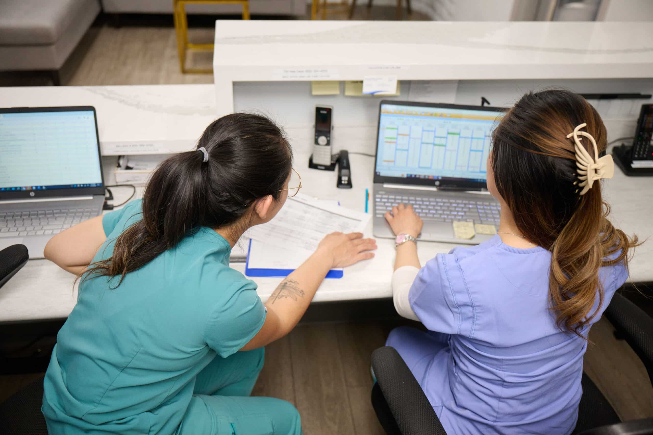 Two women in scrubs staring at a computer monitor